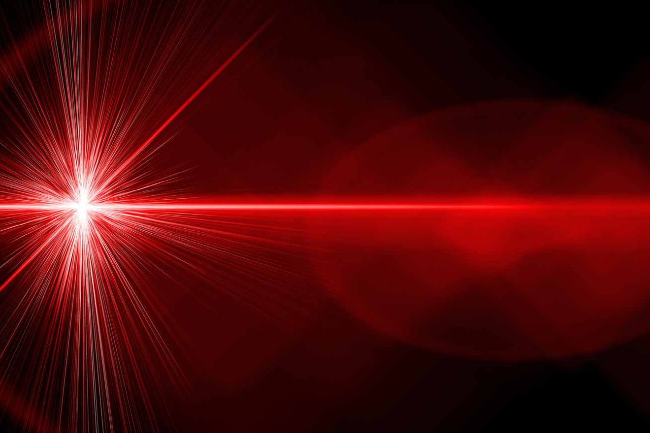 Ein roter Laserstrahl trifft gebuendelt auf einen Punkt