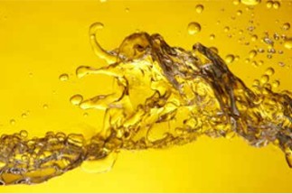 Eine goldgelbe Fluessigkeit spritzt vor gelbem Hintergrund auf