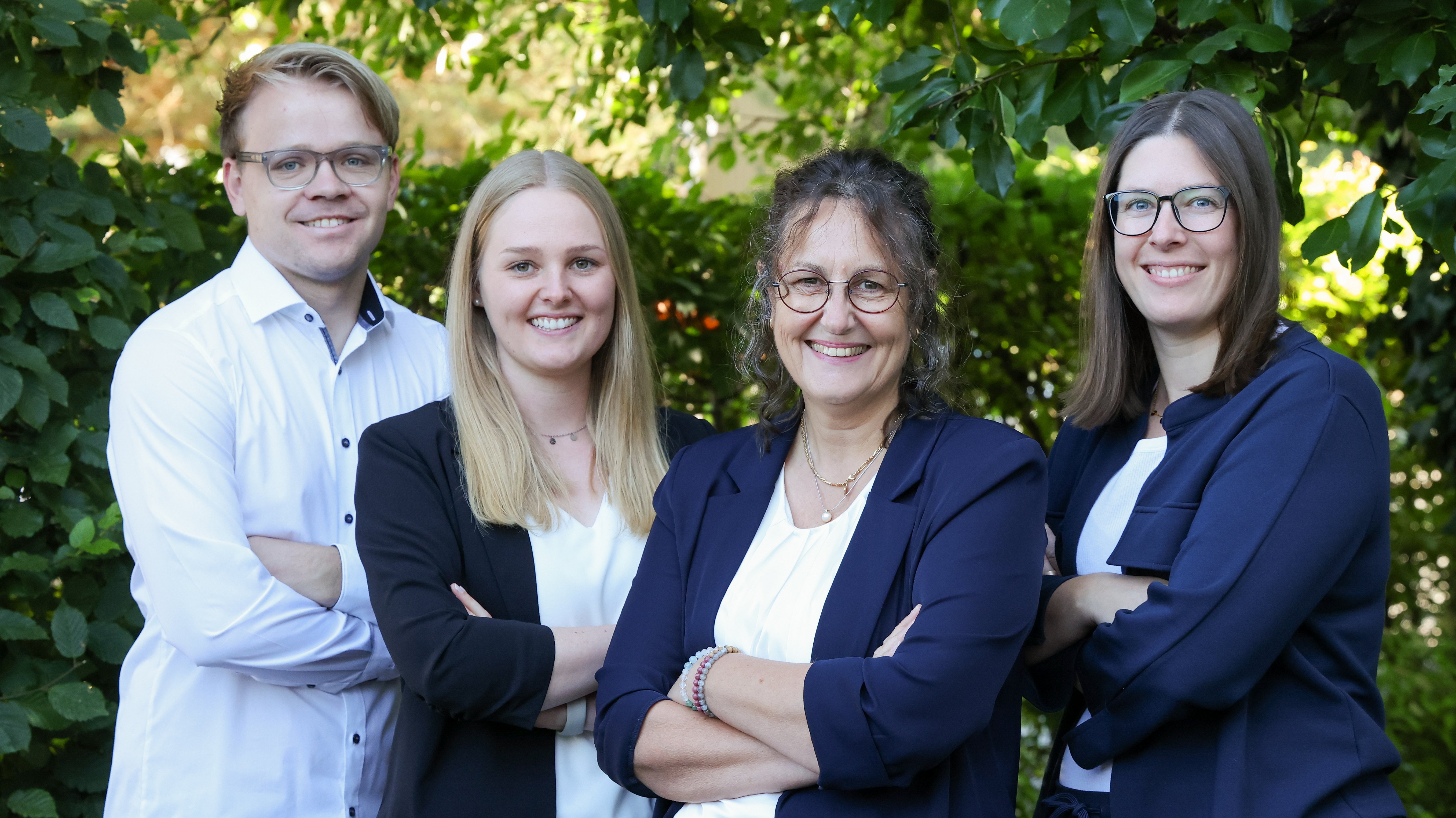 Das Team Buchhaltung von Almit, vier Personen vor einer Hecke