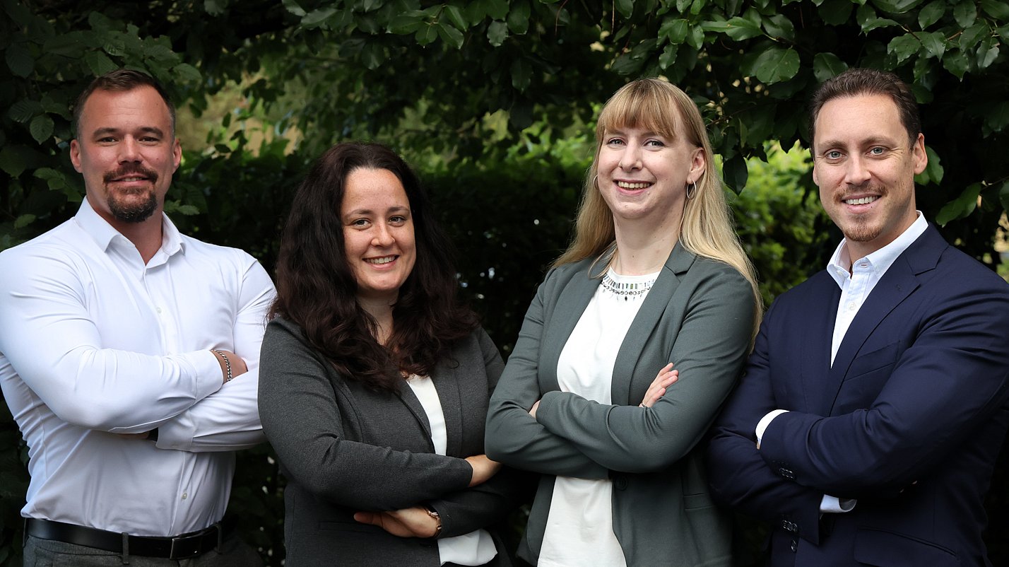 Das Team Marketing von Almit, vier Personen vor einer Hecke