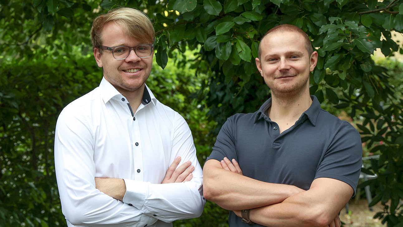 Das Team IT von Almit, zwei Personen vor einer Hecke