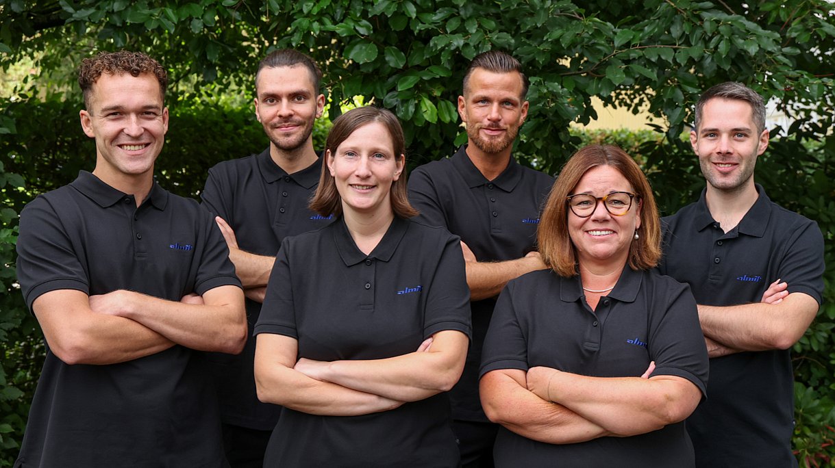 Das Team Lager von Almit, sechs Personen in dunklen Almit-Poloshirts vor einer Hecke